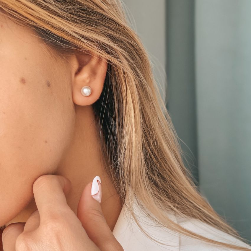 Close-up of a person wearing a classic pearl stud earring.