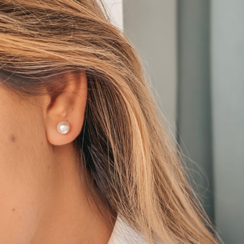 Close-up of a woman's ear wearing a classic pearl stud earring.