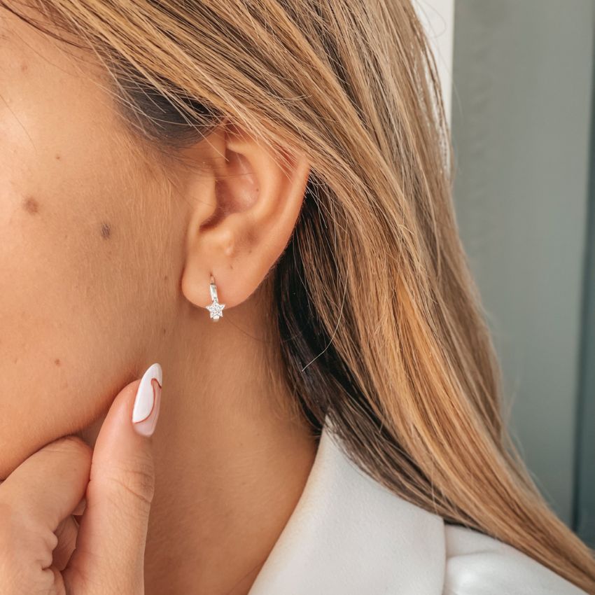 Close-up of an ear wearing a silver earring with a star-shaped zirconia and manicured hand touching the chin.