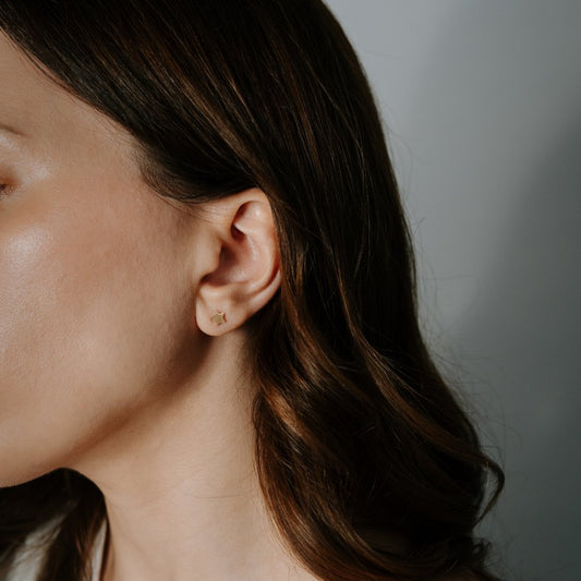 Detailní záběr na ženské ucho s náušnicí ve tvaru hvězdy z 14K zlata.