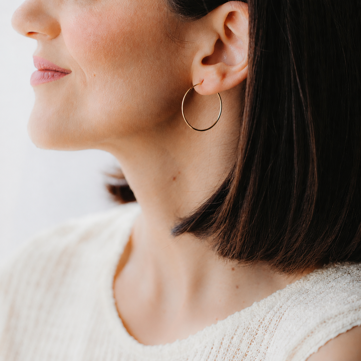 Close-up of a person wearing a medium 14K yellow gold creole hoop earring on the left ear.