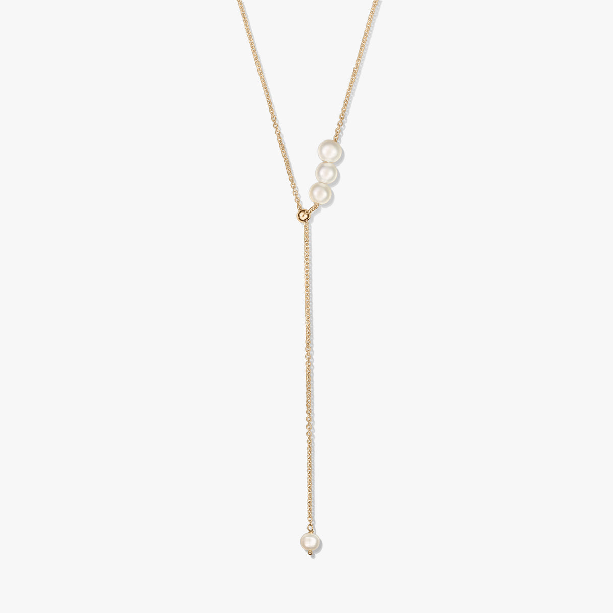 Delicate gold-plated sterling silver lariat necklace featuring a trio of cultured pearls at the slider and a single pearl drop, isolated on white.