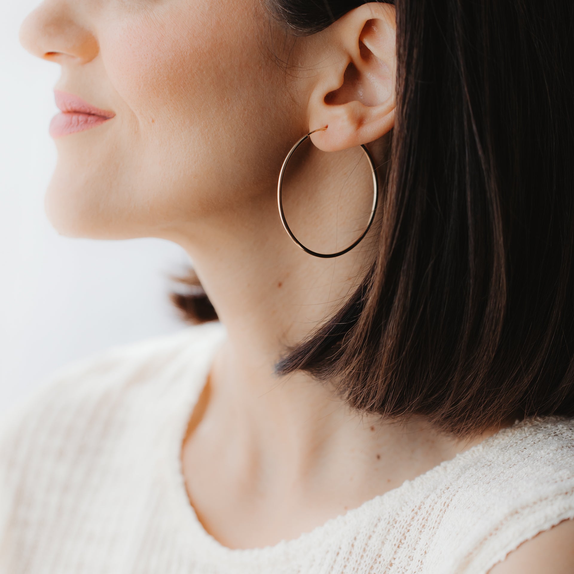 Detailní boční profil modelky s velkou kruhovou náušnicí z 14k žlutého zlata, nasazenou v uchu v měkkém přirozeném světle.