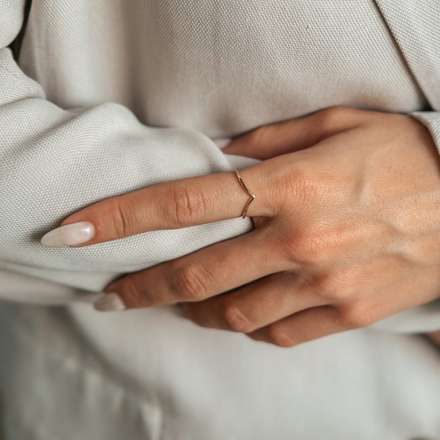 Detailní záběr na ruku s minimalistickým prstenem z pozlaceného stříbra na světle látkovém pozadí.