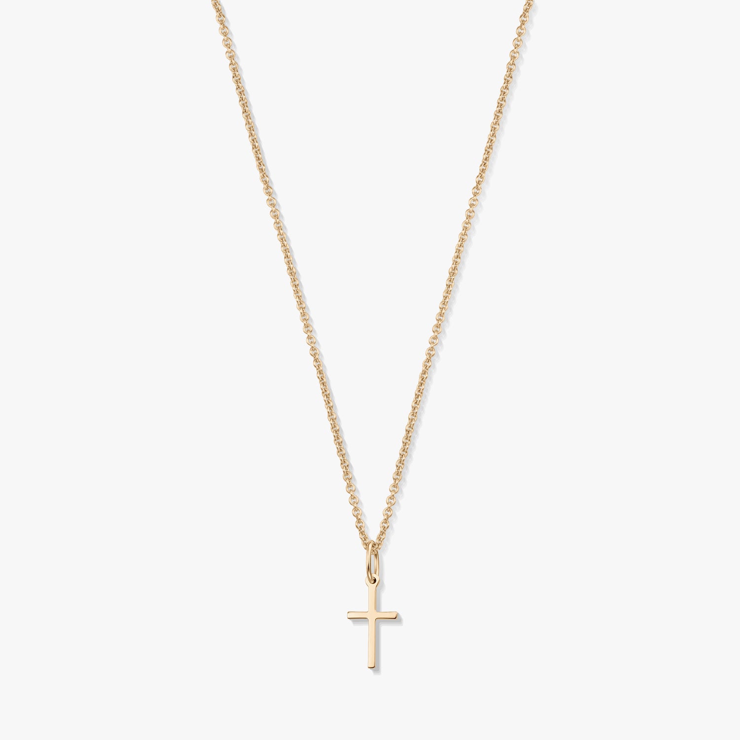 Minimalistický náhrdelník z 14K žlutého zlata s malým přívěskem křížku na jemném řetízku, izolovaný na bílém pozadí.