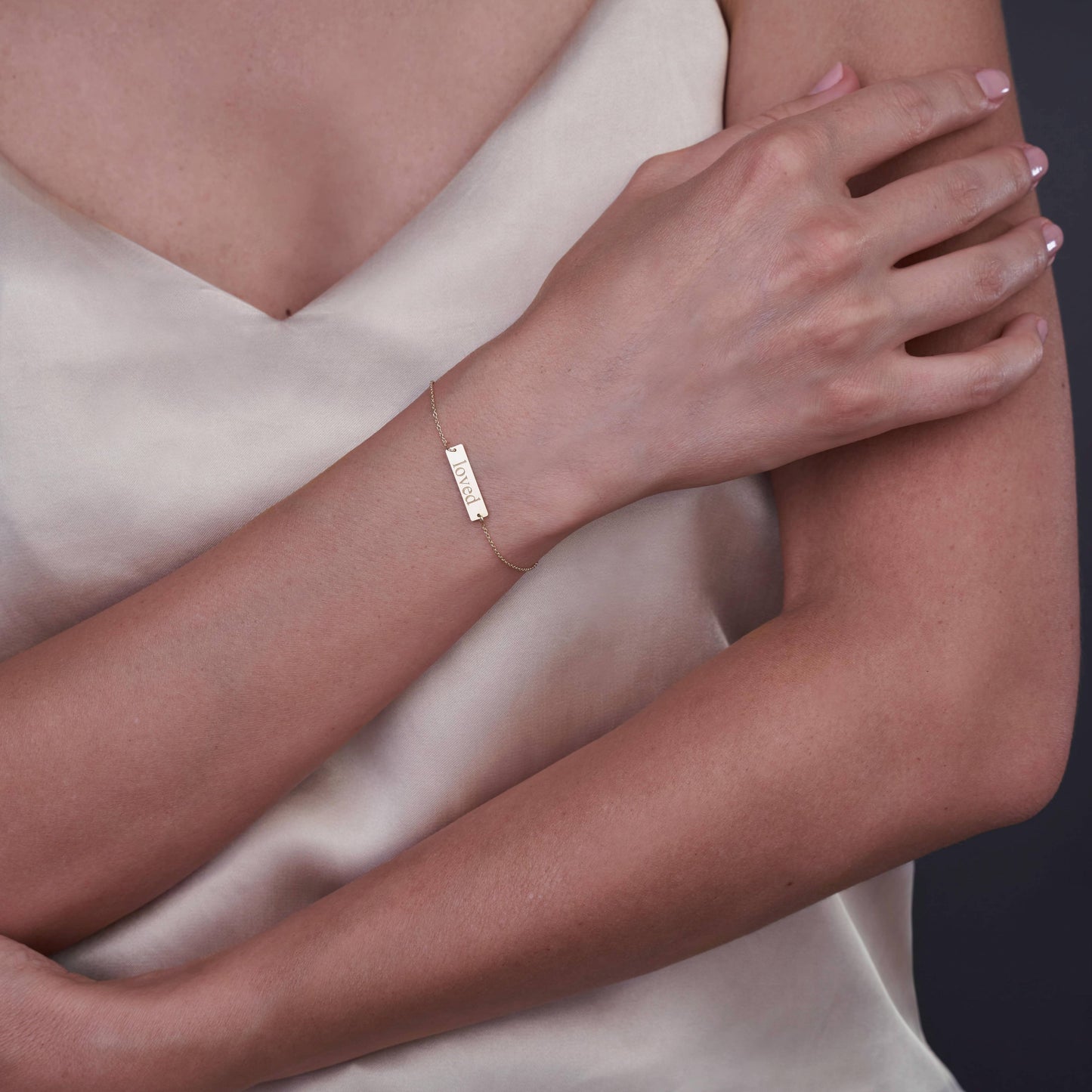 Close-up of a person wearing a 14K gold bracelet with the word 'Loved' engraved, set against a neutral background.