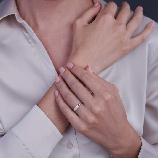 Close-up of a woman's hands wearing a gold ring with a moonstone and zirconia, against a neutral background.