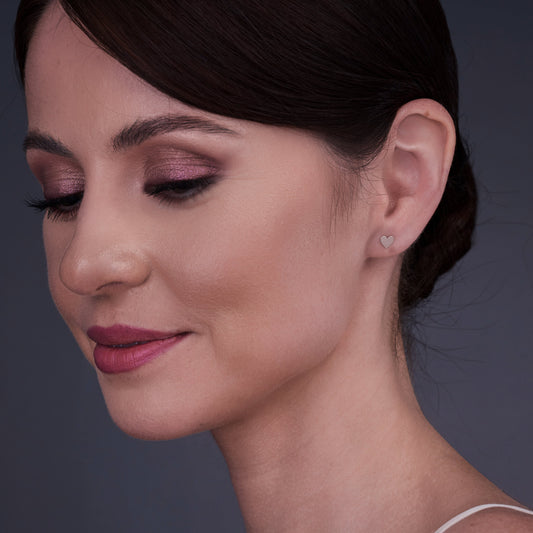 Žena nosící srdcové náušnice ze 14K zlata se zavřenýma očima a klidným výrazem.