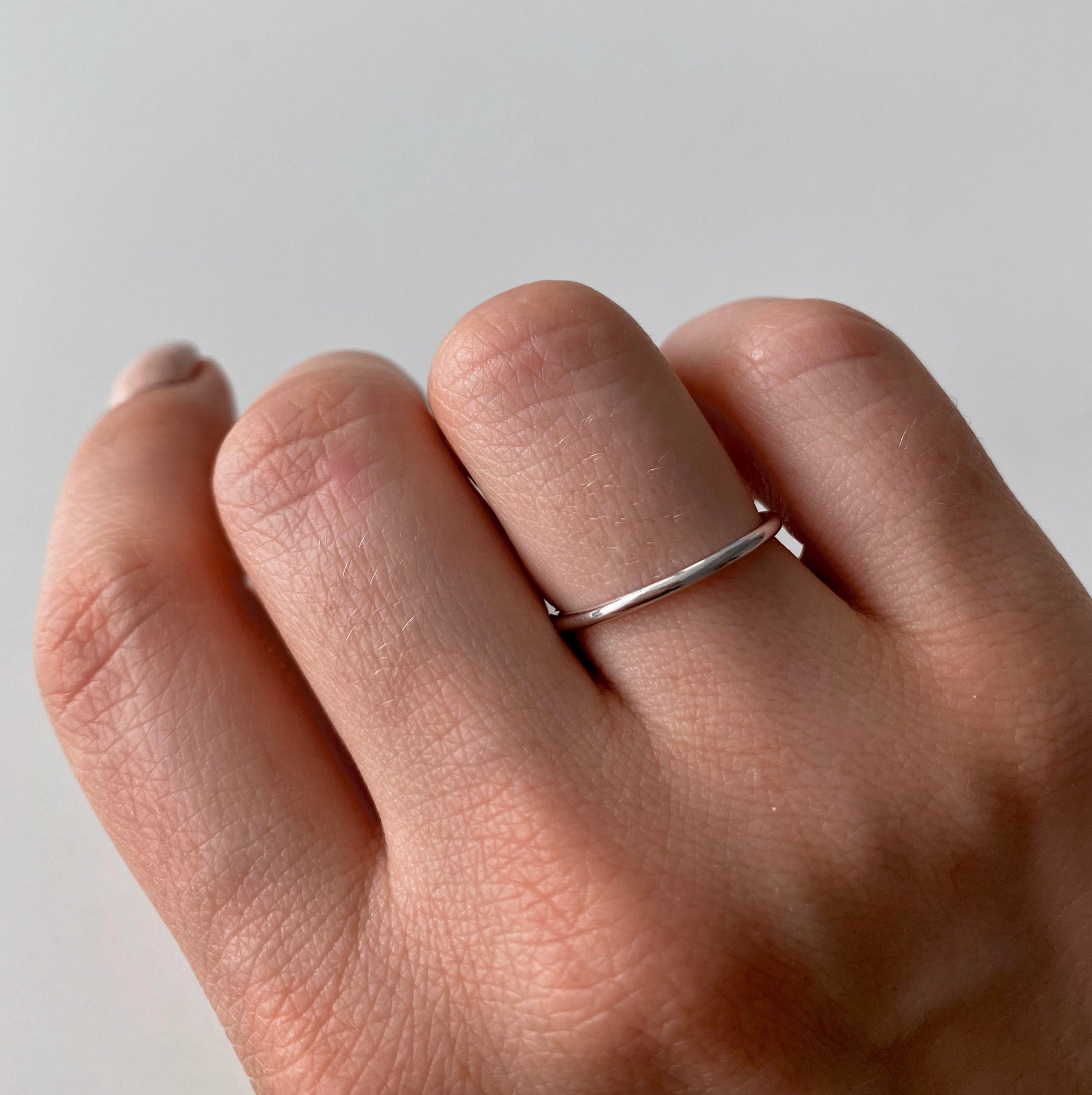 A hand wearing a simple silver ring with a light background.