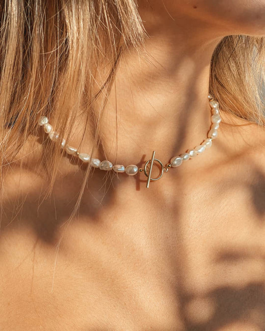 Close-up of a woman's neck wearing a silver necklace with natural pearls and a gold clasp.