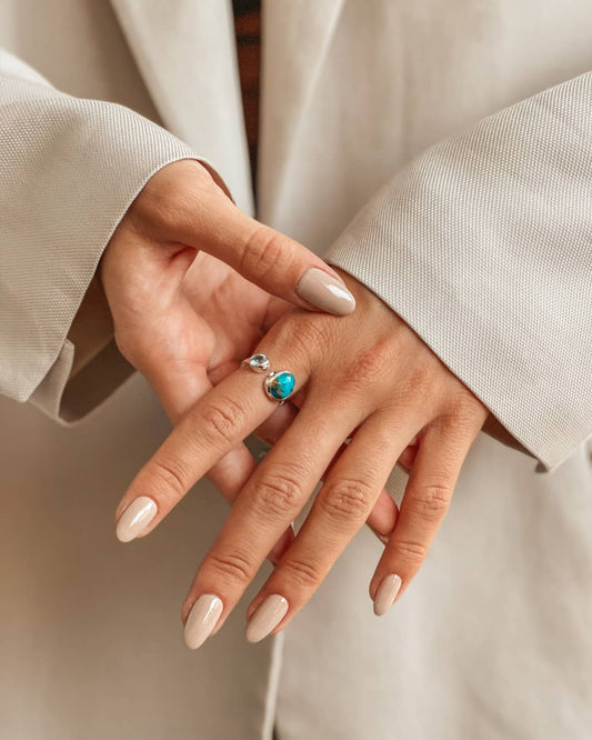 Close-up of hands displaying a silver ring with blue topaz and turquoise stones.