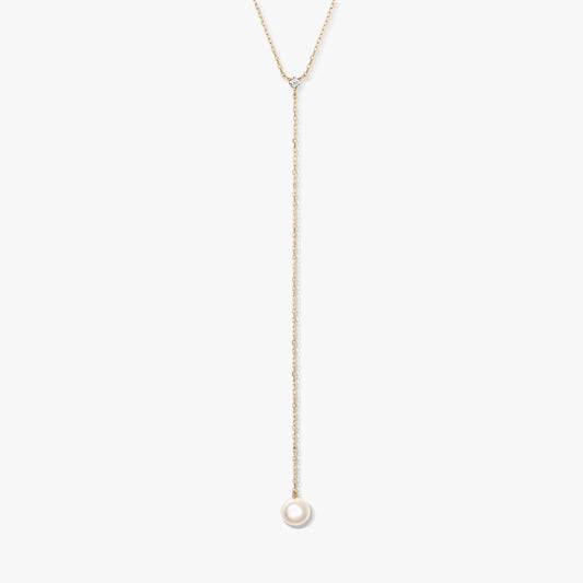 Minimalistický zlatý lariatový náhrdelník s jedinou kulatou bílou perlou ve tvaru kapky a malým doplňkovým kamínkem, vystředěný na bílém pozadí.