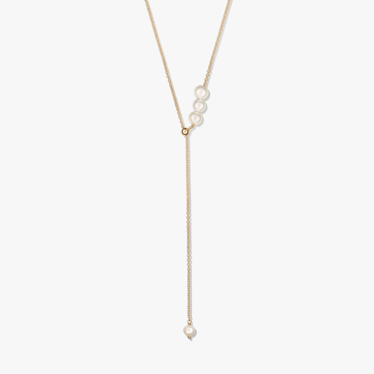 Delicate gold-plated sterling silver lariat necklace featuring a trio of cultured pearls at the slider and a single pearl drop, isolated on white.