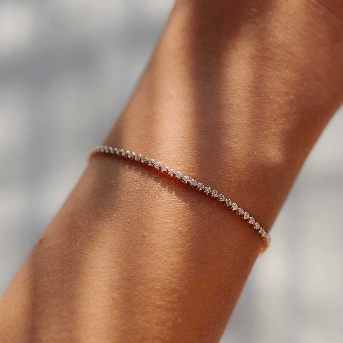 Close-up of a delicate 14K yellow gold tennis bracelet with small round diamonds worn on a wrist, lit by soft natural light.