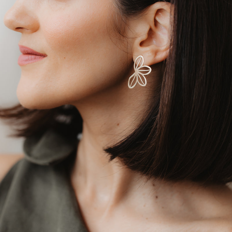 Close-up of a model wearing the Half Wildflower 14K yellow gold stud earring with an open-petal design; soft indoor light and neutral background.