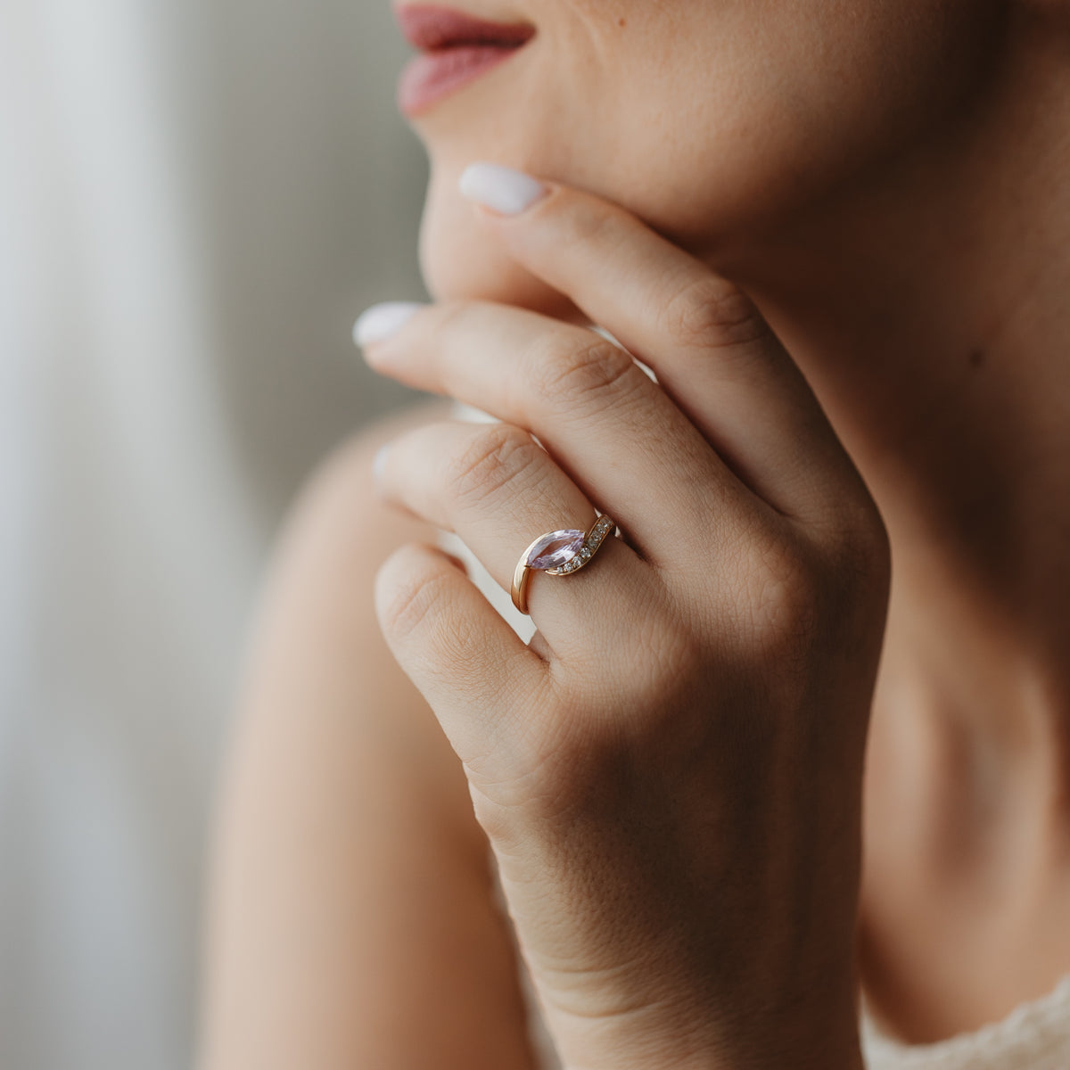 Detailní záběr ruky u obličeje s prstenem Velvet Rose ze žlutého zlata 14K s růžovým safírem ve tvaru markýzy a drobnými akcentními diamanty.