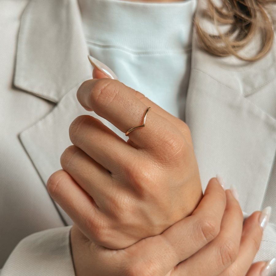 Osoba nosící jednoduchý zlatý prsten ve tvaru V na prstu, oblečená ve světlém obleku.