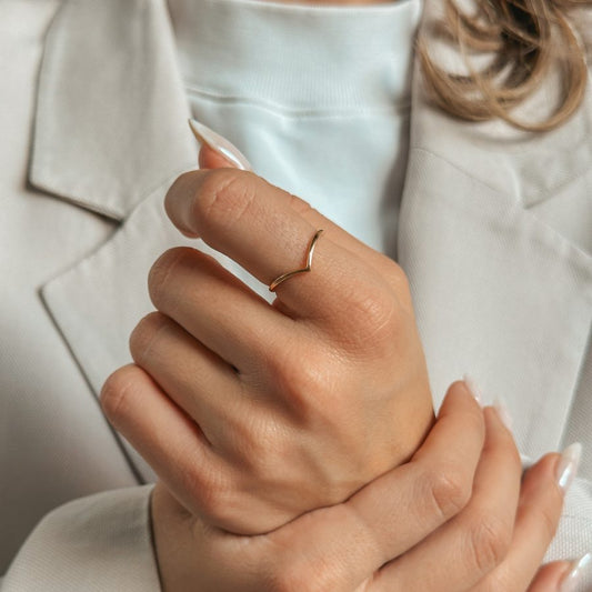 A person wearing a simple V-shaped golden ring on their finger, dressed in a light suit.