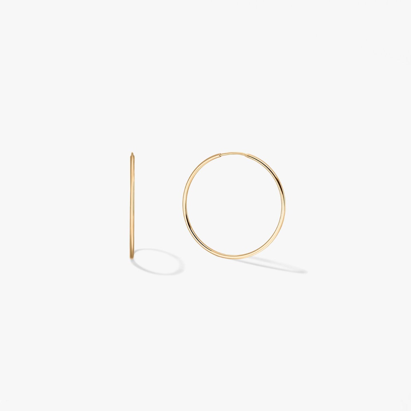 Pair of mini 14k yellow gold hoop earrings on a white background, one shown front-on and one in side profile.