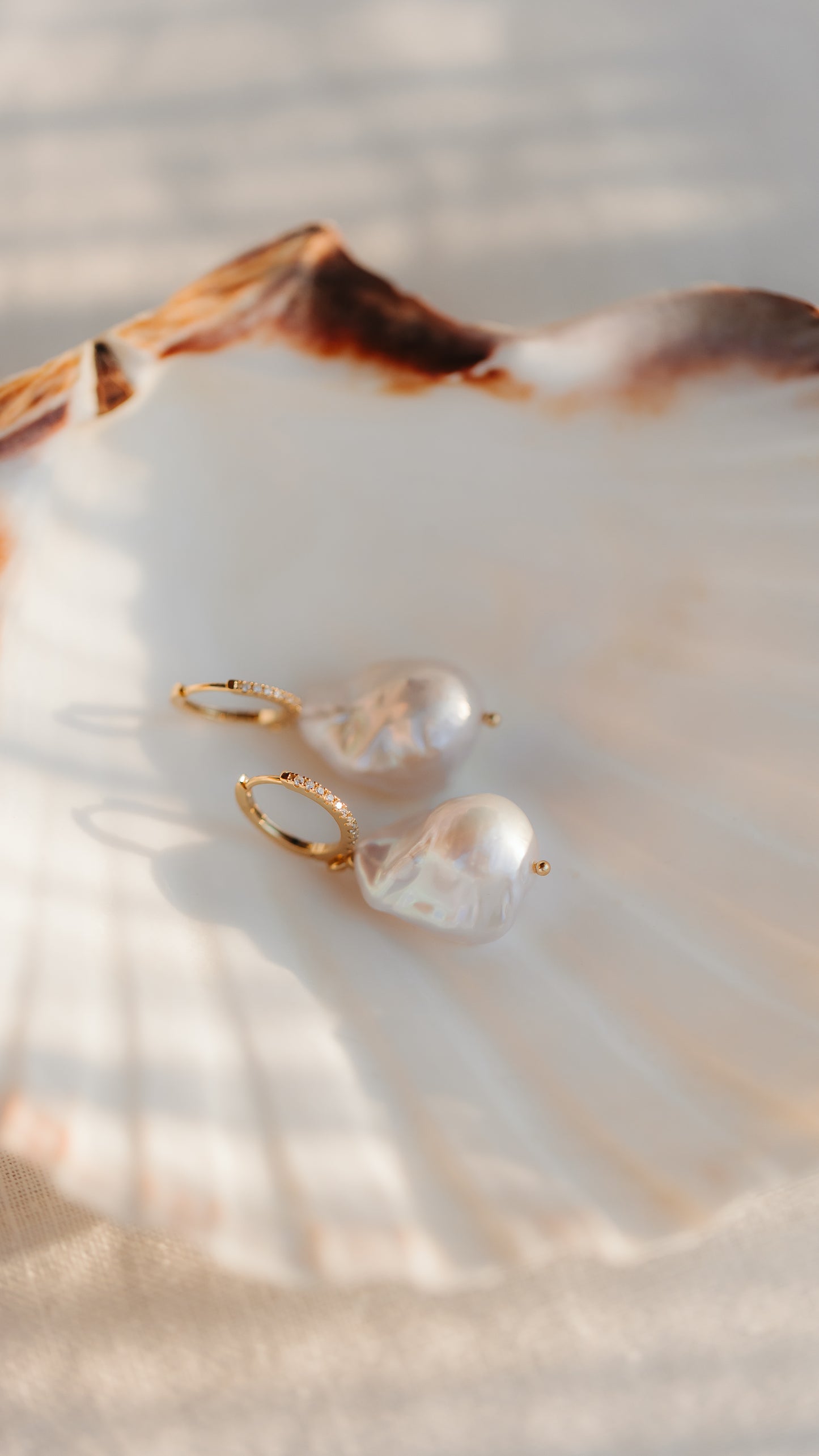 Gold‑plated 925 silver hoop earrings with large baroque pearls, styled on a scallop shell in warm natural light.