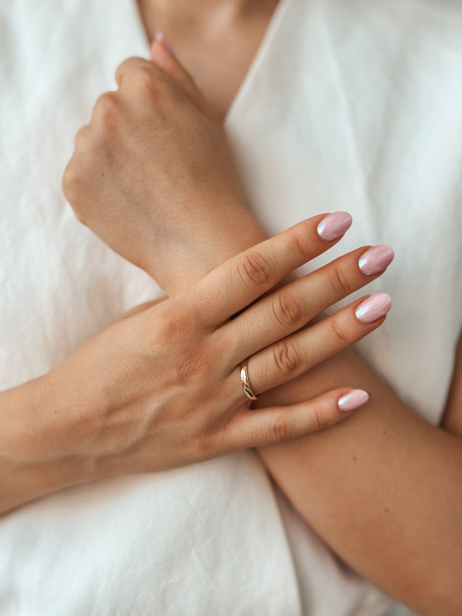 Close-up of a hand wearing a wide rounded gold wedding band with pink and silver nail art.