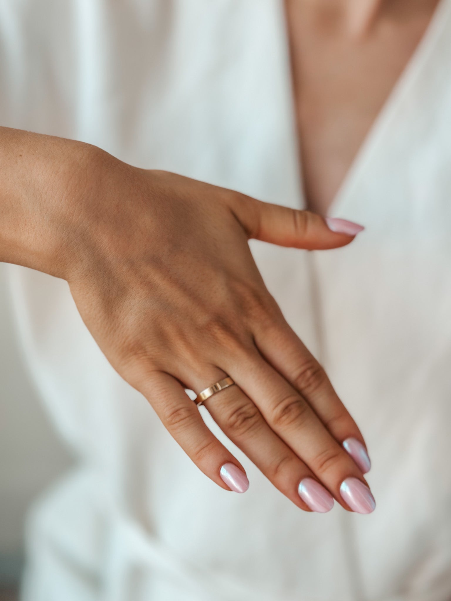 A hand showcasing a simple gold wedding band with pink manicured nails.