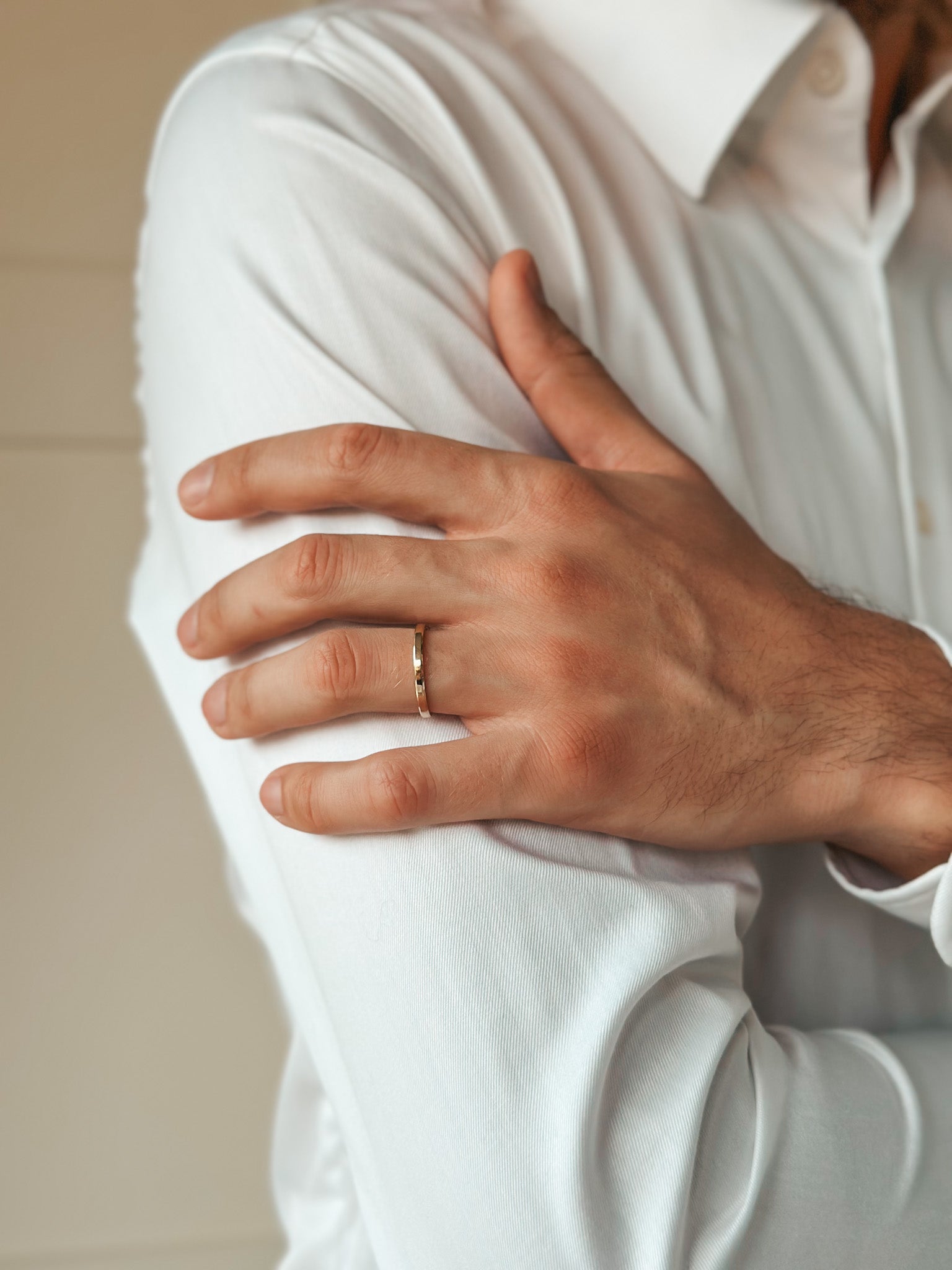 Close-up of a hand wearing a gold wedding ring on the arm of a white shirt.