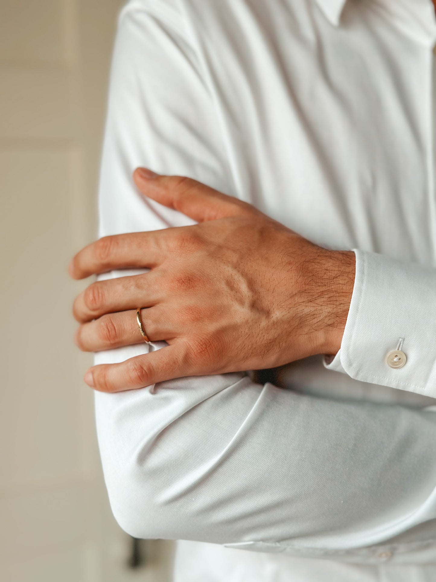 Close-up of a person wearing a white shirt and a thin gold wedding band on their finger.
