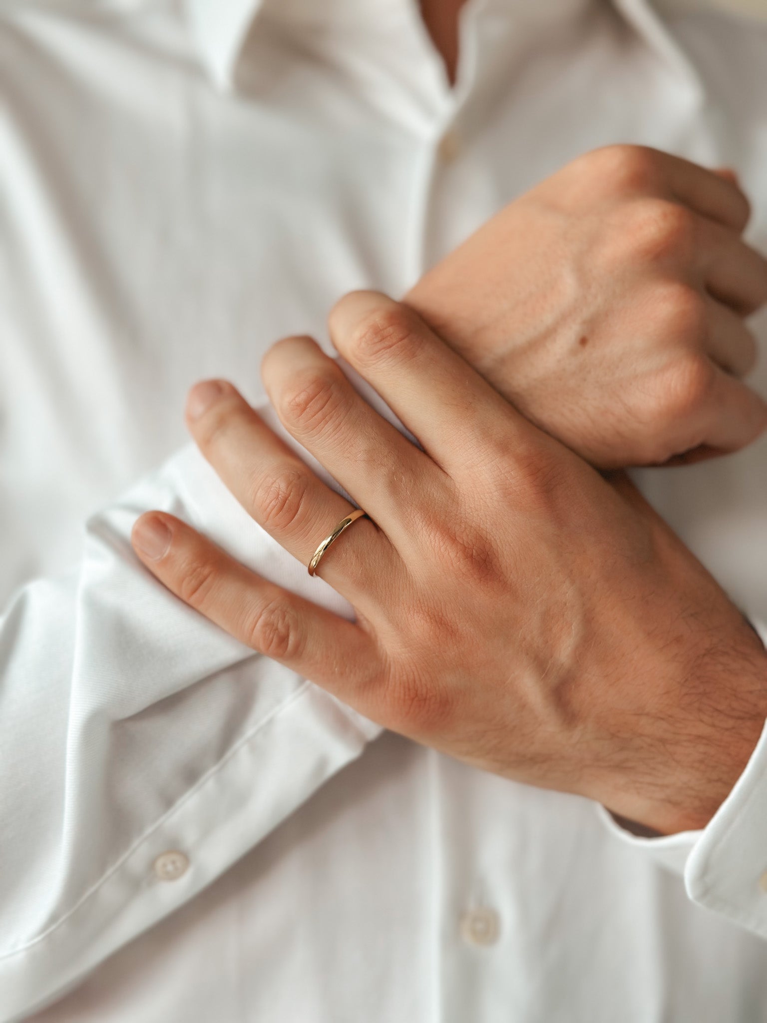Close-up of a person wearing a thin rounded gold wedding band on their hand over a white shirt.