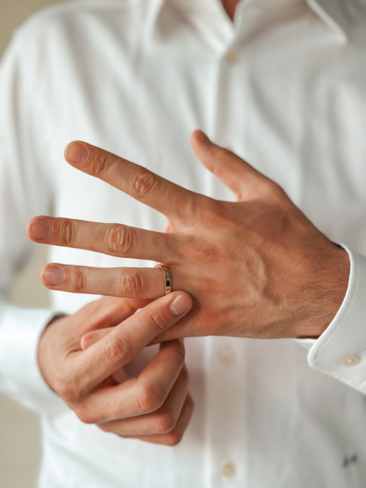 A person in a white shirt putting on a simple gold wedding band on their finger.