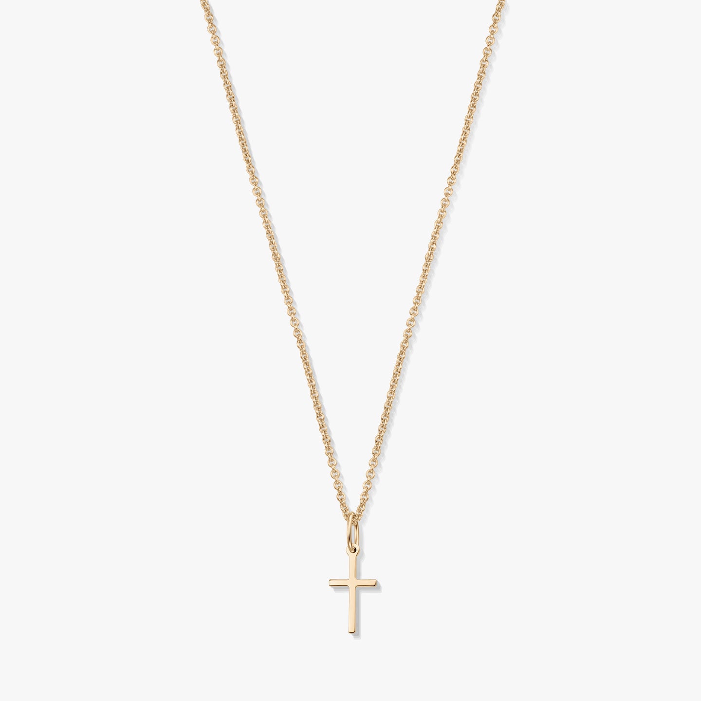 Minimalistický náhrdelník z 14K žlutého zlata s malým přívěskem křížku na jemném řetízku, izolovaný na bílém pozadí.