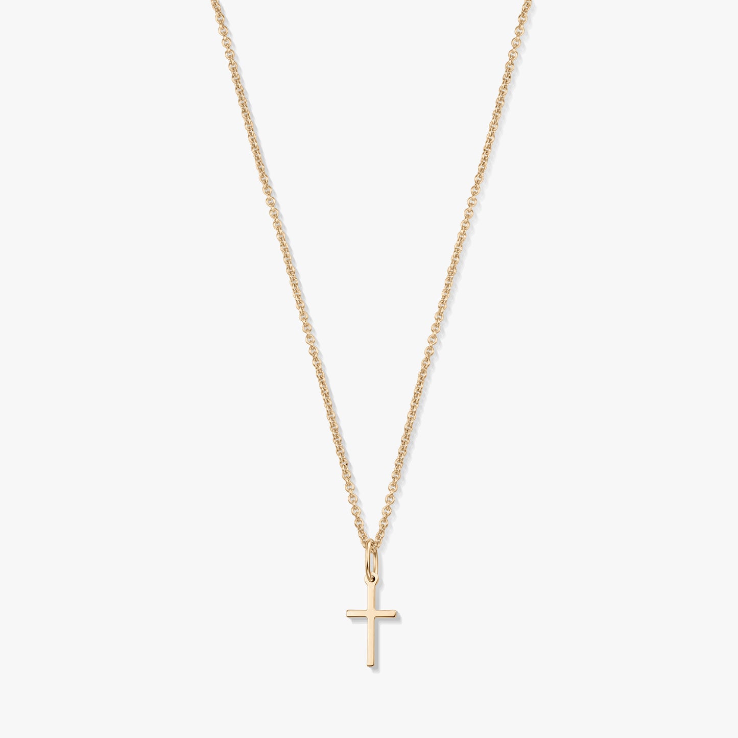 Minimalistický náhrdelník z 14K žlutého zlata s malým přívěskem křížku na jemném řetízku, izolovaný na bílém pozadí.