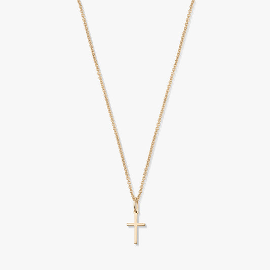 Minimalistický náhrdelník z 14K žlutého zlata s malým přívěskem křížku na jemném řetízku, izolovaný na bílém pozadí.
