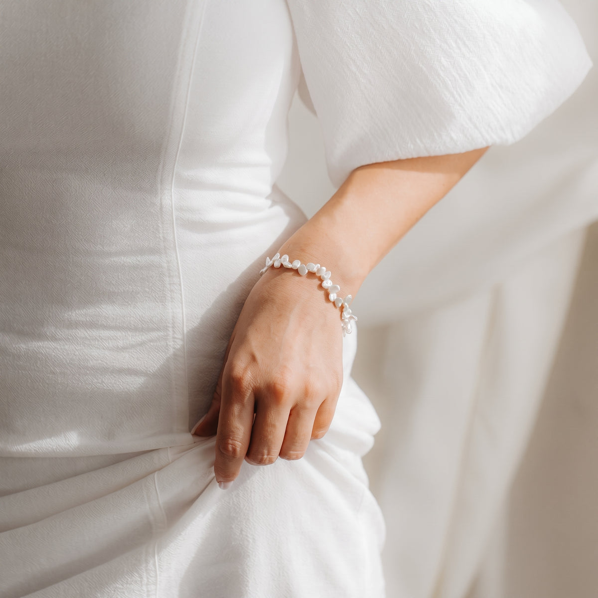 Close-up of a wrist wearing a Keshi pearl bracelet on gold‑plated sterling silver, styled with a white dress in soft natural light.
