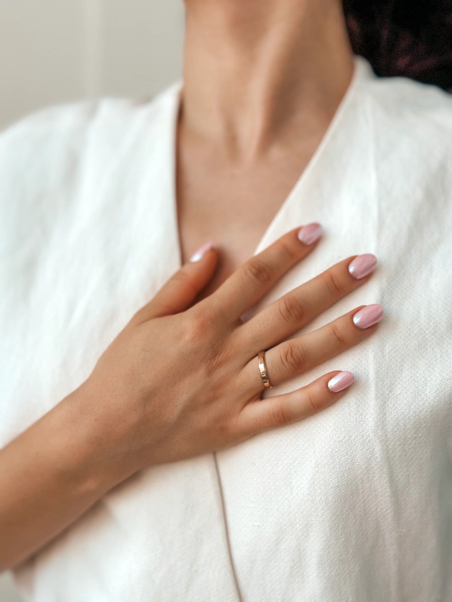 Close-up of a hand with manicured nails resting on a chest, wearing a wide gold wedding band.