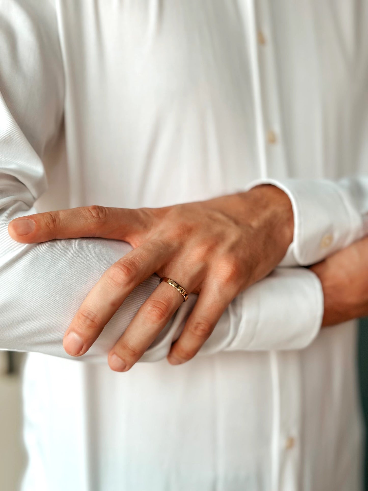 Close-up of a person wearing a white shirt, showcasing a gold wedding band on their hand.