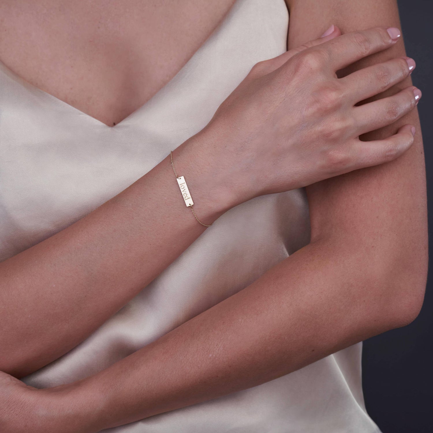 Close-up of a person wearing a 14K gold bracelet with the word 'Loved' engraved, set against a neutral background.
