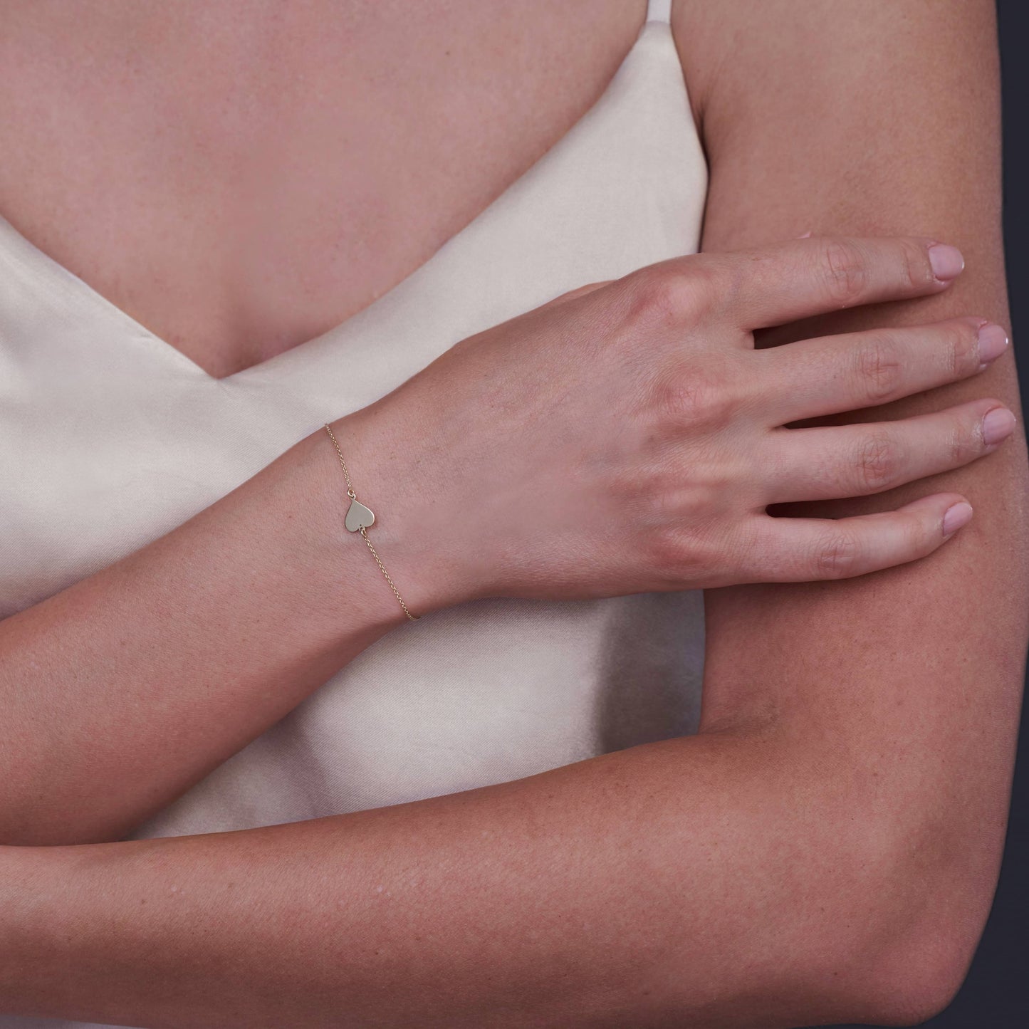Close-up of a wrist wearing a 14K gold heart bracelet with a minimalist design.
