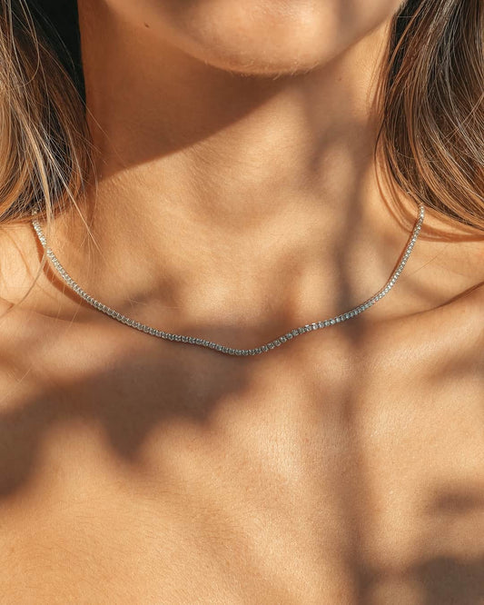 Close-up of a person wearing a silver tennis necklace with zirconia in soft lighting