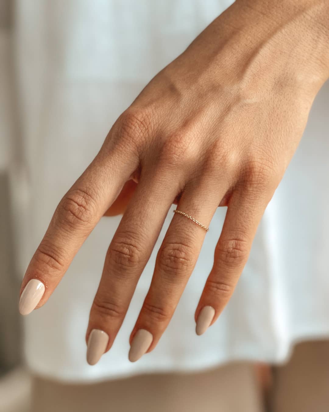 A delicate hand wearing a 14K gold chain ring with nude manicured nails.